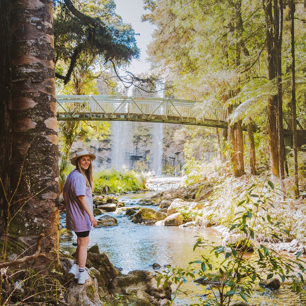 Woman stands in front of New Zealand waterfall scene